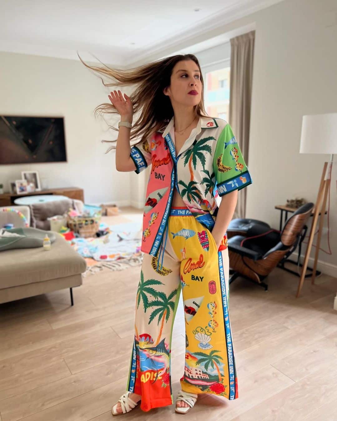 Elise standing in her living room, looking away from the camera and flipping her hair. She is wearing a brightly colored multi patterned outfit.
